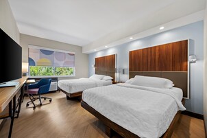 Habitación de hotel con dos camas, un escritorio, una silla y un televisor.