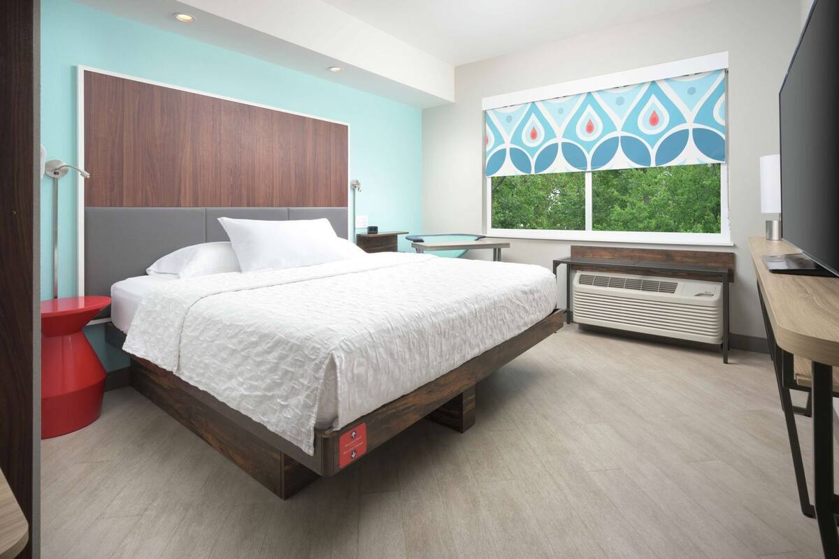 A modern bedroom with a bed, bedside table, heater, and a window with a view.