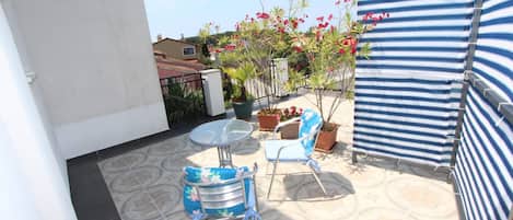 A patio area with a round table and two chairs, a striped awning, and potted plants.