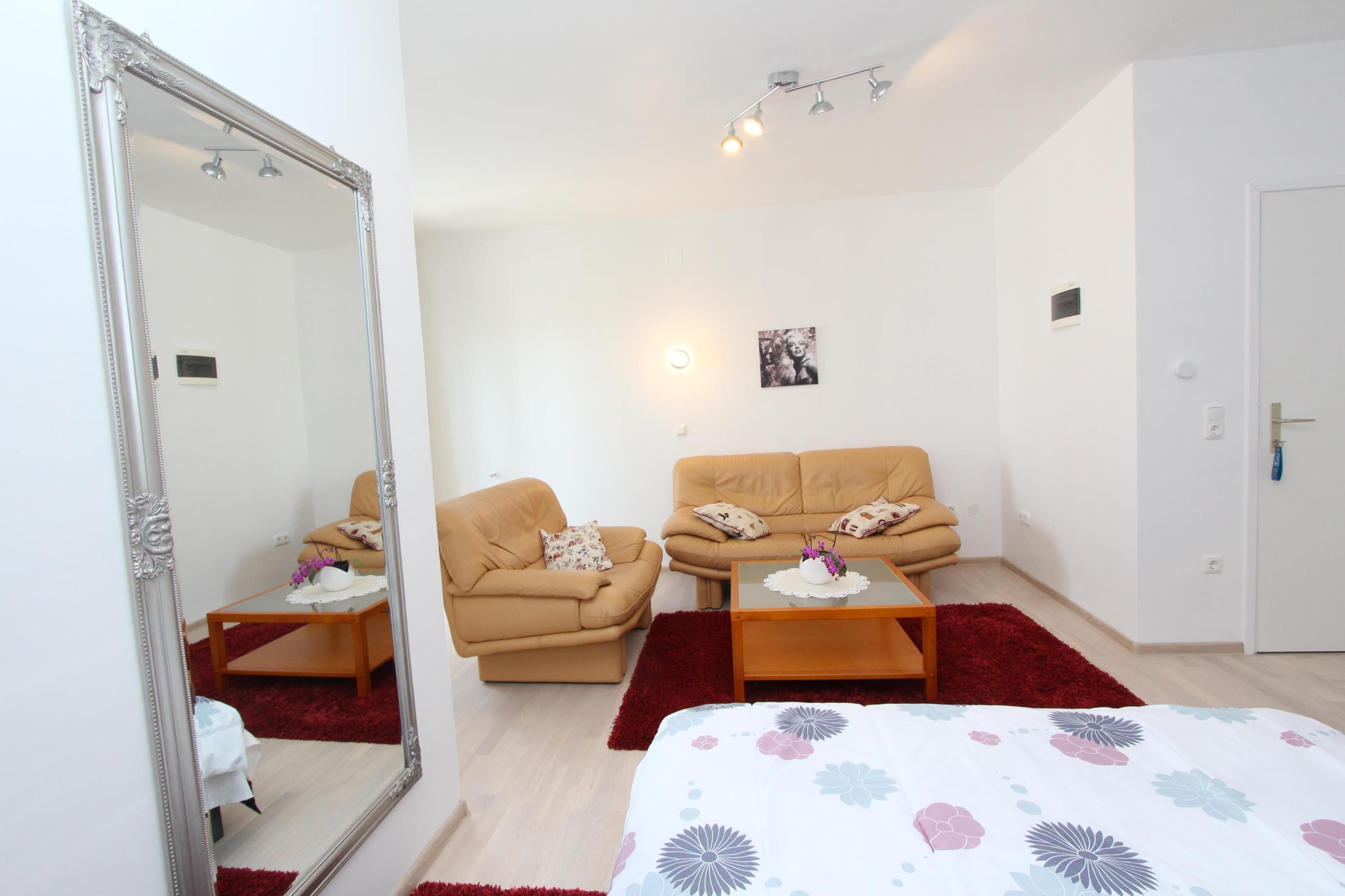 Una habitación moderna con un espejo grande, dos sofás, una cama y una pequeña mesa con un florero.