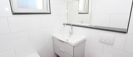 Un baño moderno con azulejos blancos, un lavabo blanco con un espejo encima, una bañera y un inodoro.