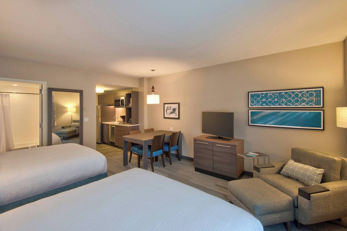 Une chambre d’hôtel avec deux lits, un bureau avec une chaise, un canapé, une télévision et une petite table.