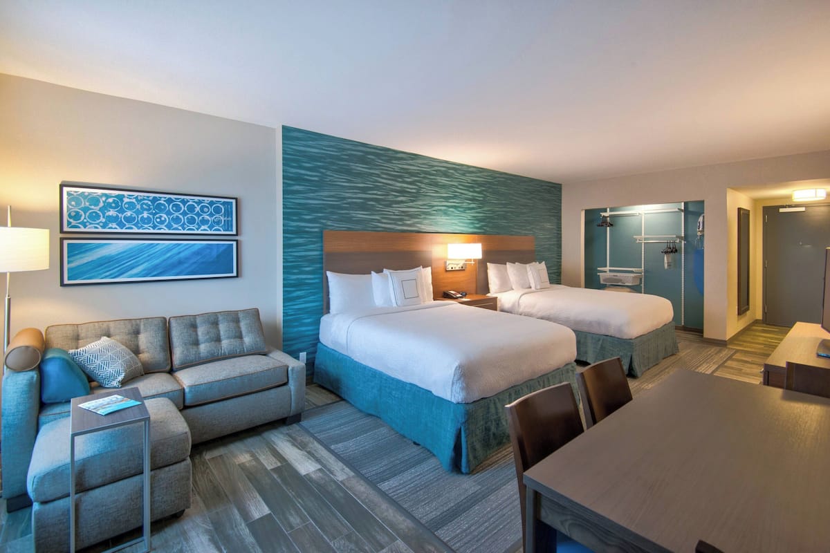 Une chambre d’hôtel avec deux lits, un canapé, une table et une salle de bain visible à travers une porte ouverte.