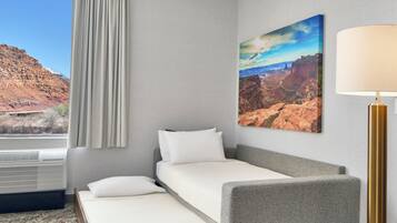 Habitación de hotel con cama, mesita de noche, lámpara, un cuadro y ventana con cortinas.