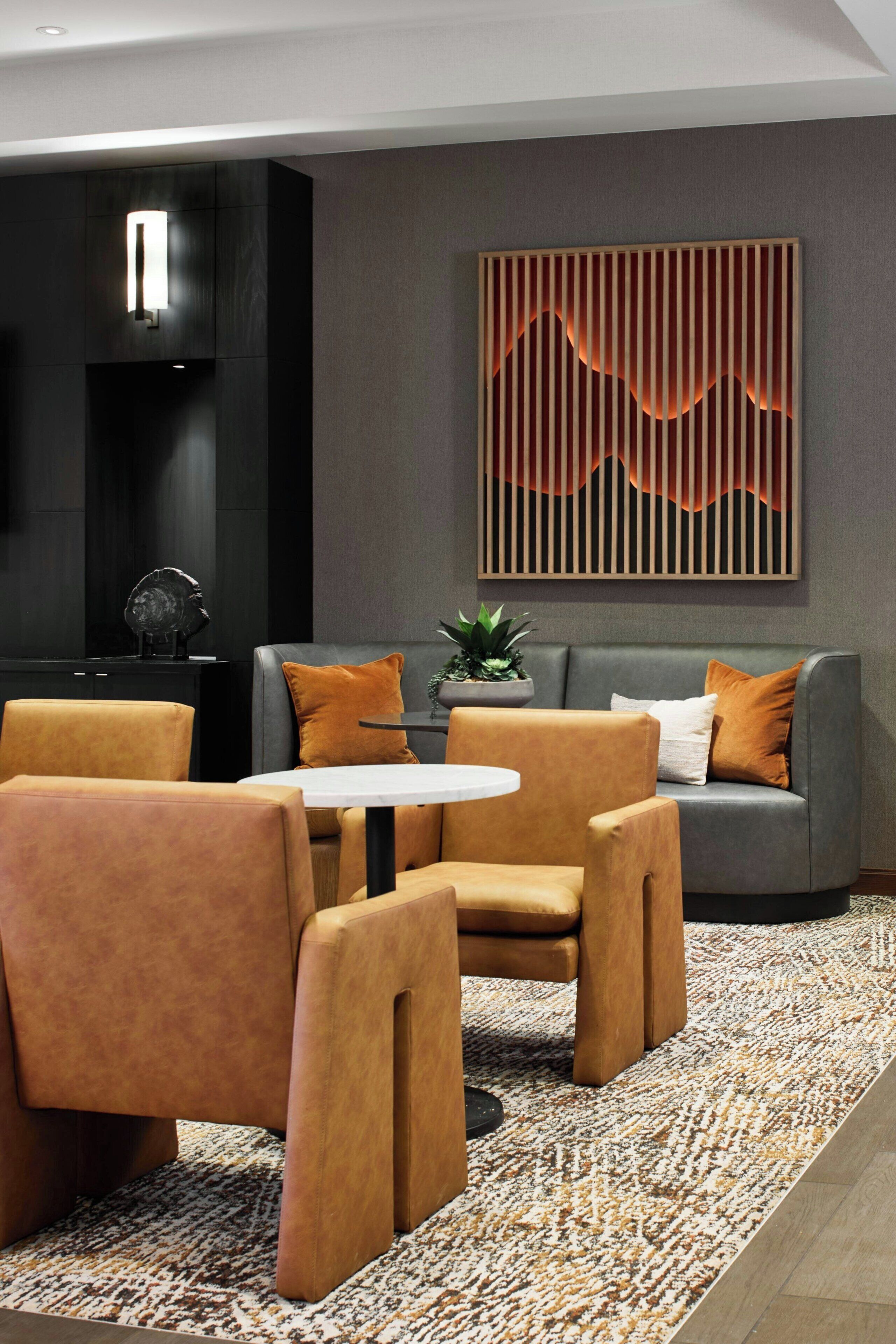 Ein modernes Interieur mit einer Couch, zwei Sesseln, einem kleinen Tisch, einer Wanddekoration und einem Blumentopf.