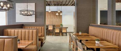A restaurant interior with booth seating, wooden tables, pendant lighting, and a central dining area.