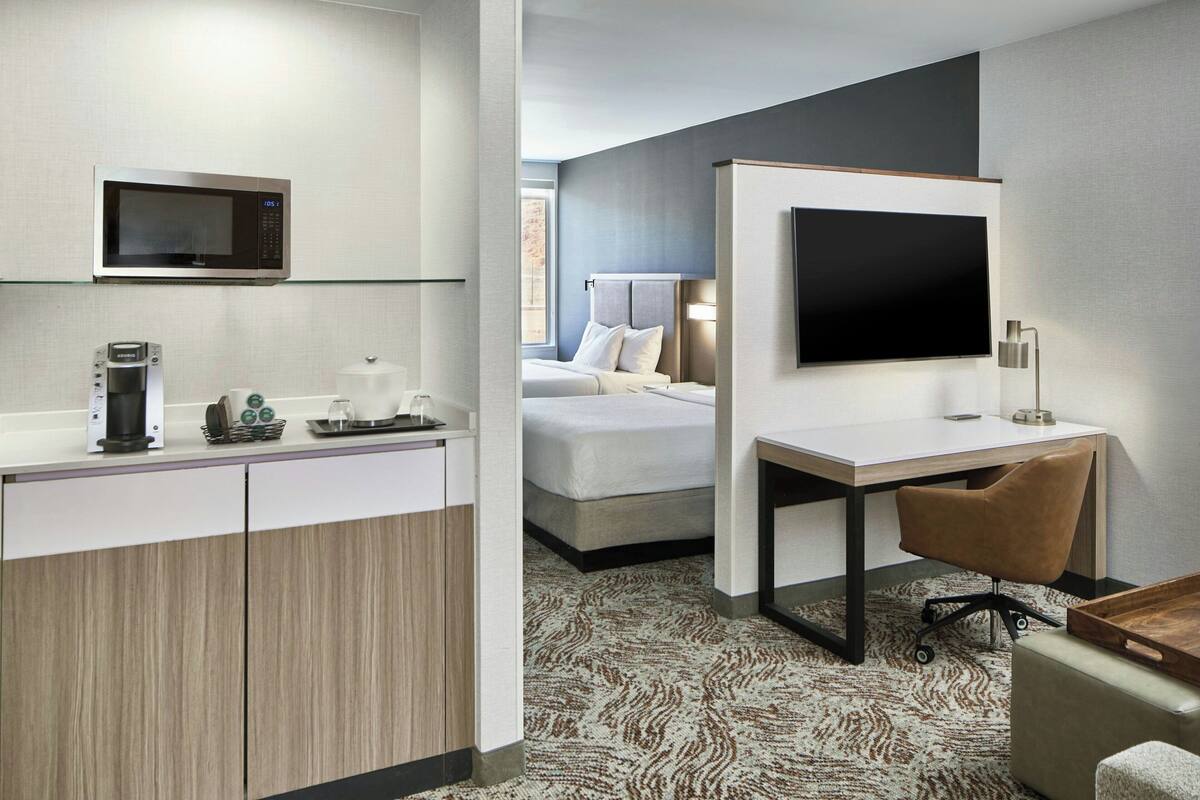 A hotel room with a kitchenette, a bed, a TV, a desk, and a chair.