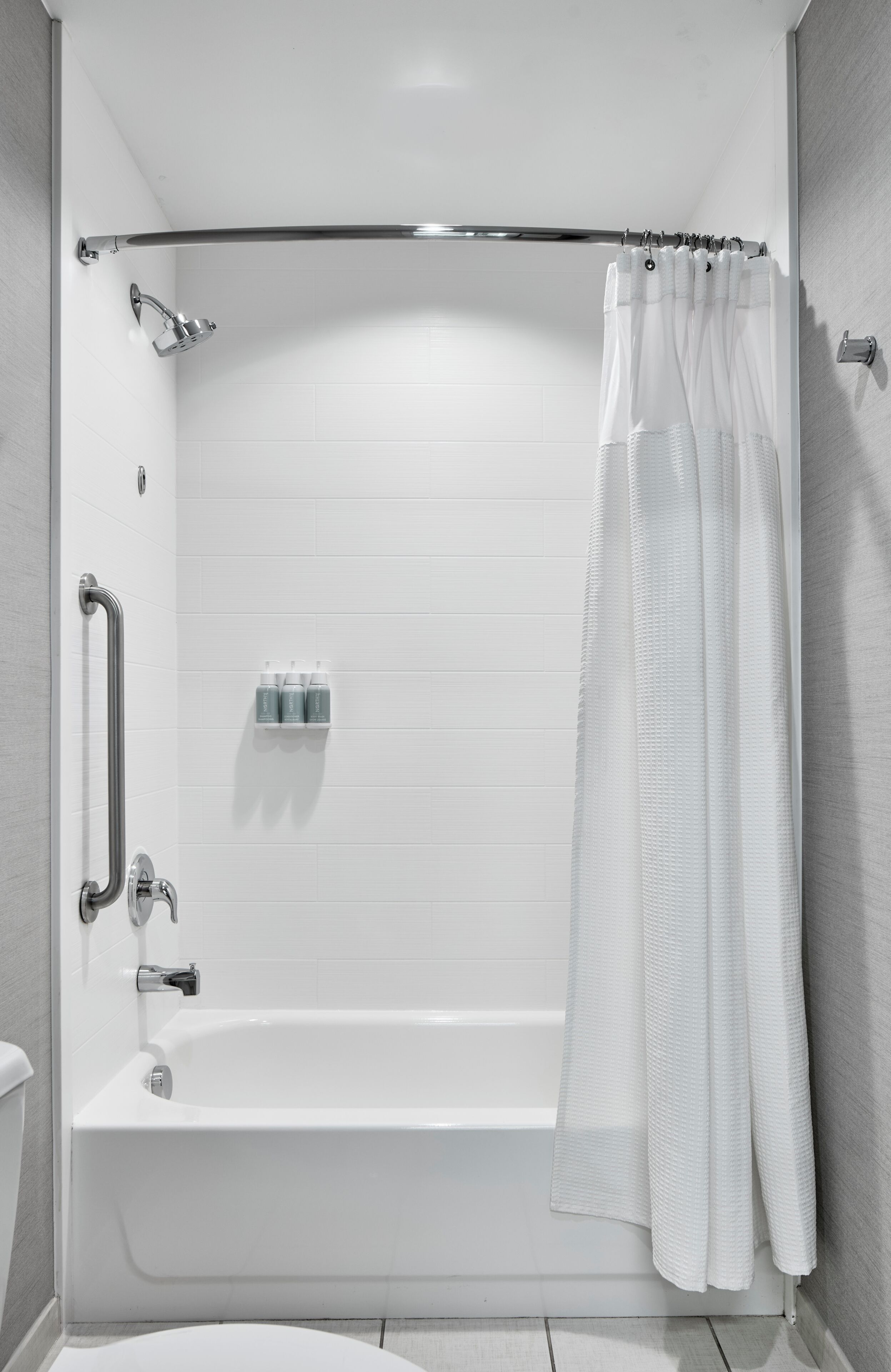 Un baño moderno con una bañera blanca, un cortinón de ducha y un pasamanos.