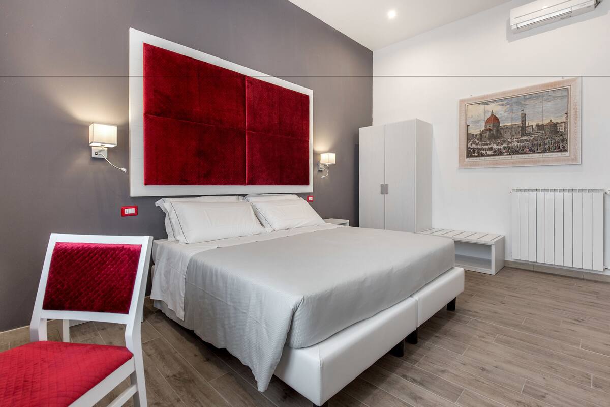 Une chambre à coucher moderne avec un grand lit, des meubles blancs et un tableau représentant un paysage urbain accroché au mur.