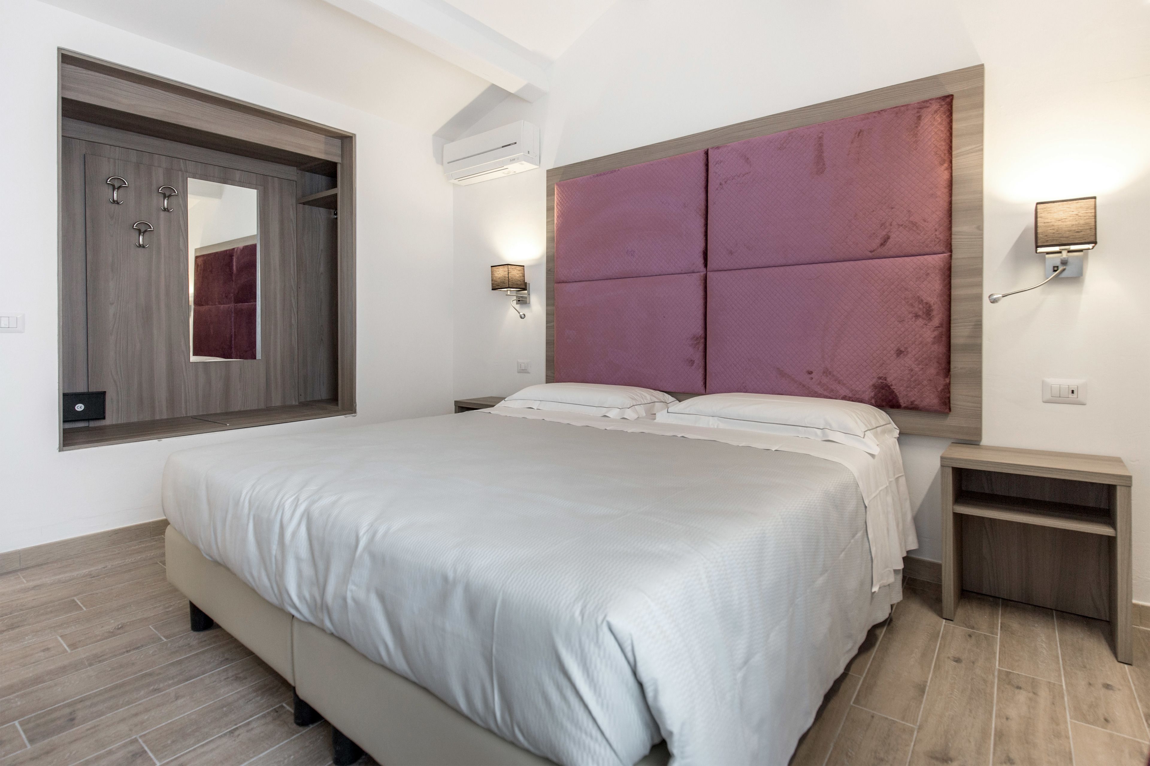 Un dormitorio moderno con una cama grande, un armario empotrado, un espejo y un aplique de pared.