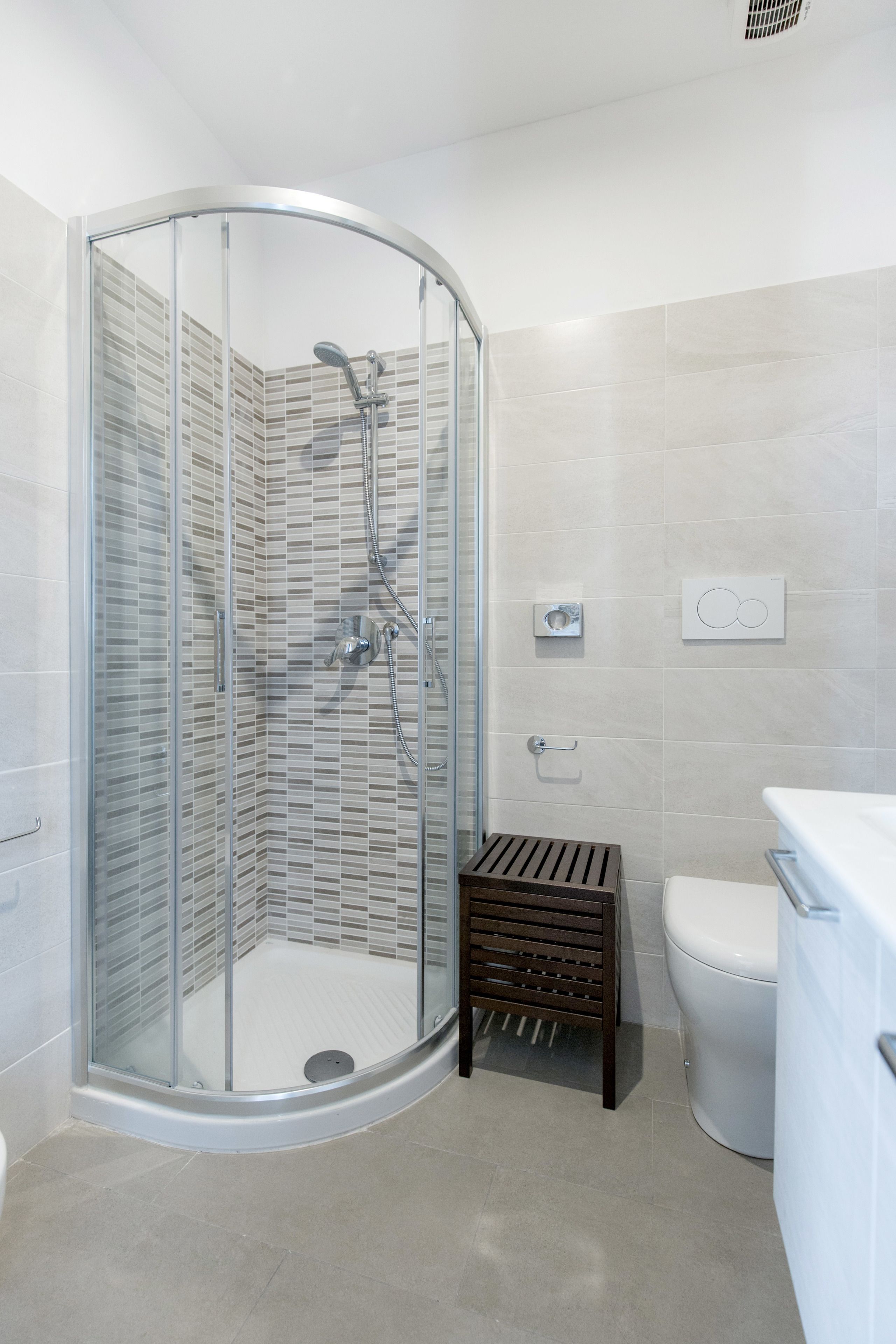 A modern bathroom with a glass-enclosed shower, a toilet, and a small wooden stool.