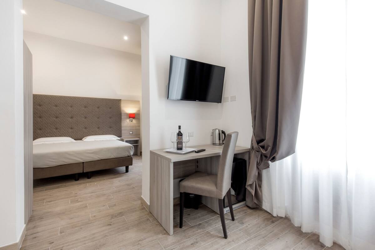 Une chambre d’hôtel comprenant un lit, un bureau avec une chaise, un téléviseur à écran plat et une fenêtre avec des rideaux.