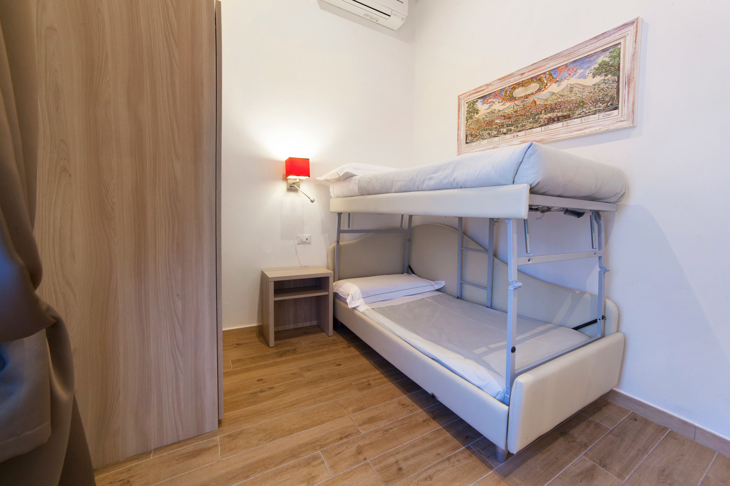 A bunk bed room with a small bedside table and a wall-mounted lamp.
