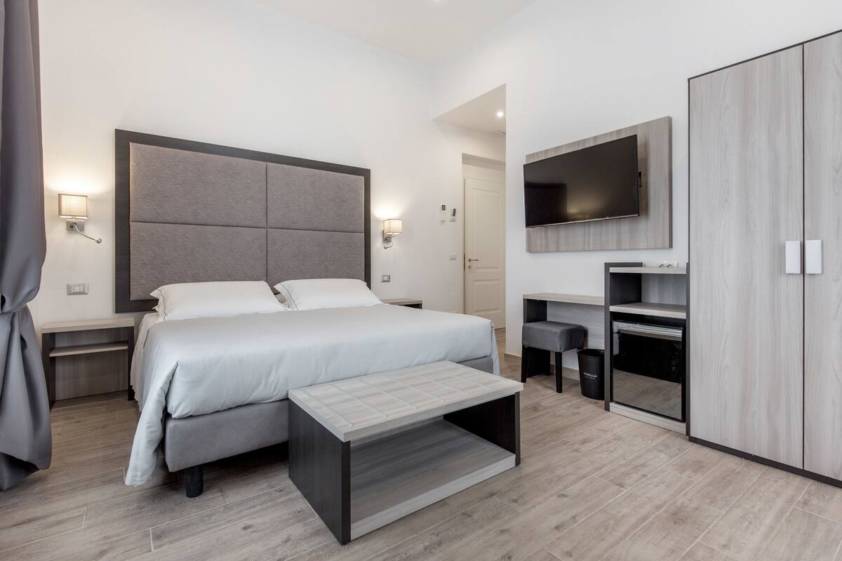 Une chambre d’hôtel moderne dotée d’un grand lit, de tables de chevet, d’une télévision, d’une armoire et d’un bureau avec une chaise.