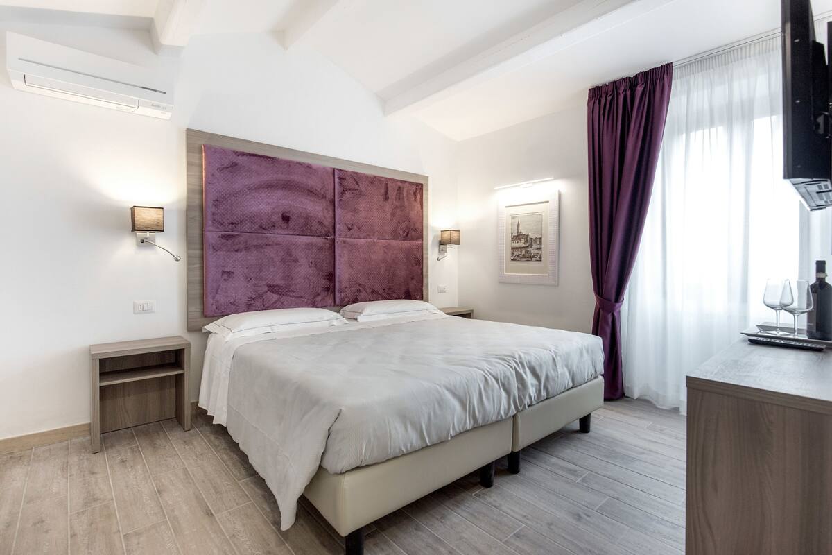 Une chambre à coucher moderne avec un grand lit, des tables de chevet, une tête de lit et une fenêtre avec des rideaux.