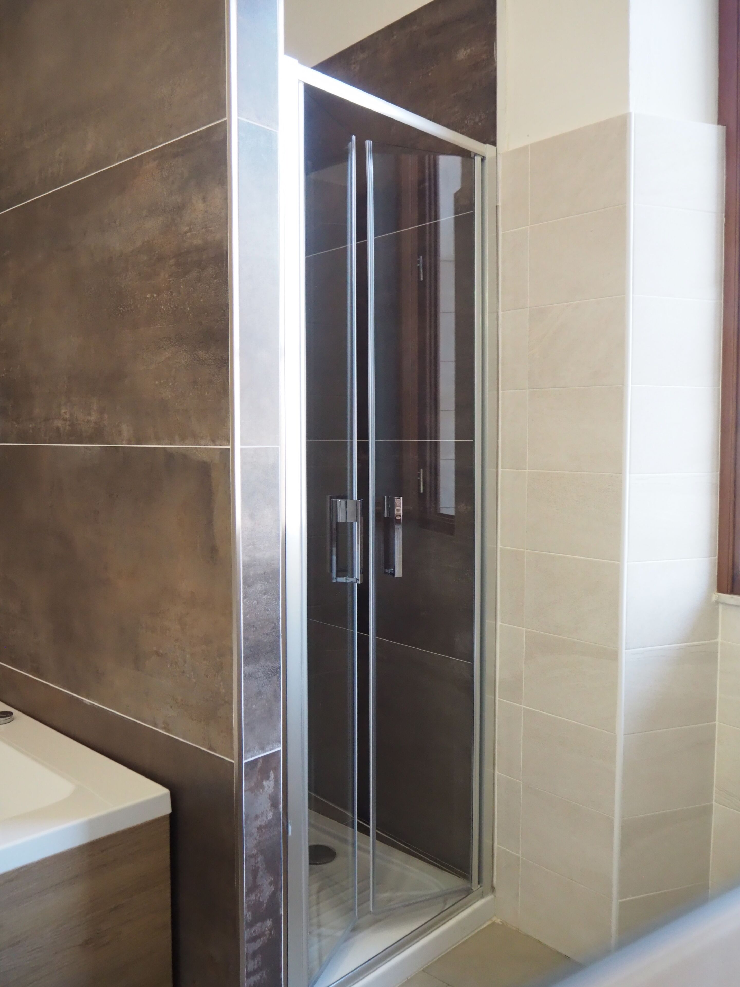 A modern bathroom with a glass-enclosed shower, dark brown tiles, and a white sink.