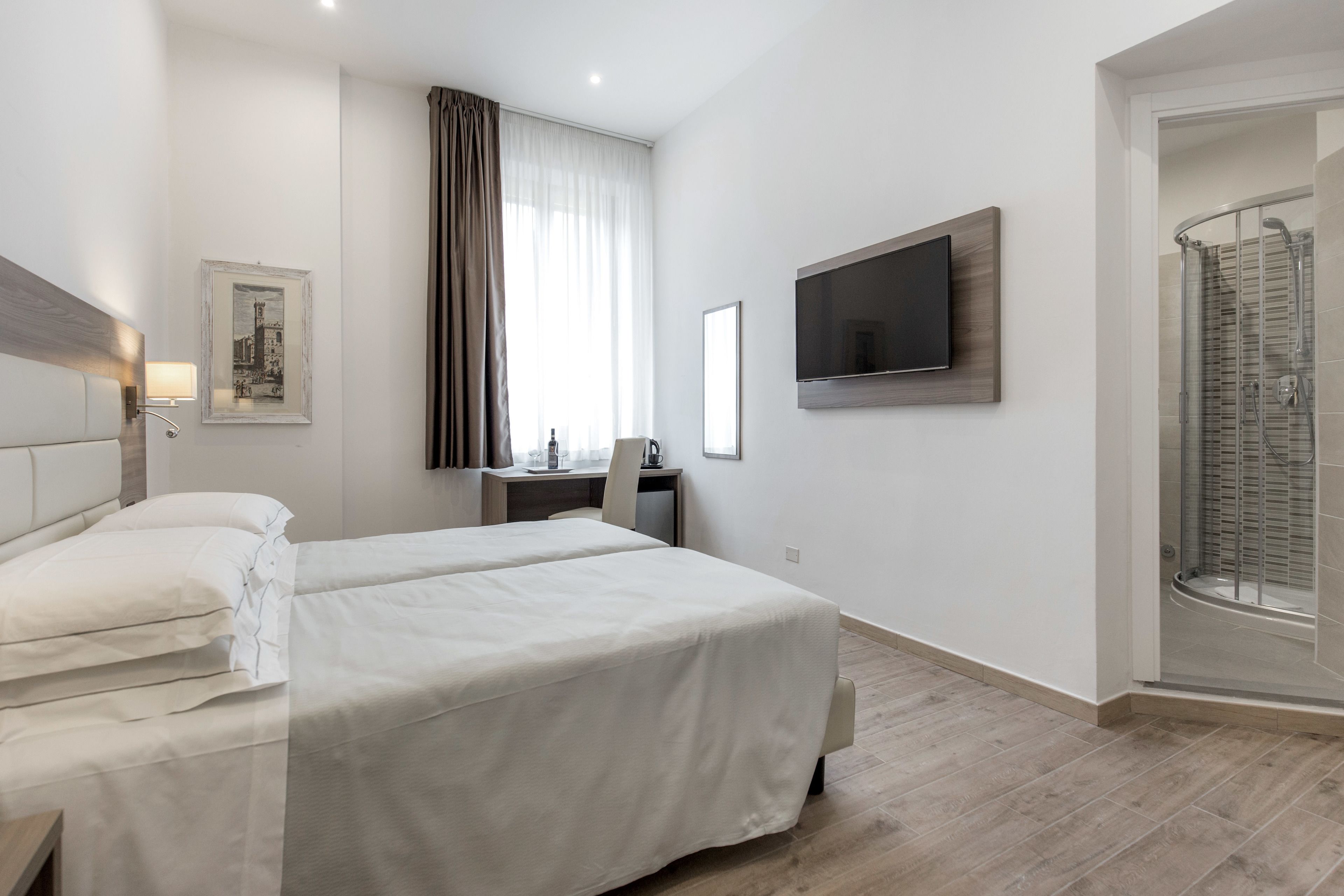 A hotel room with two beds, a desk, a TV, and a shower area.