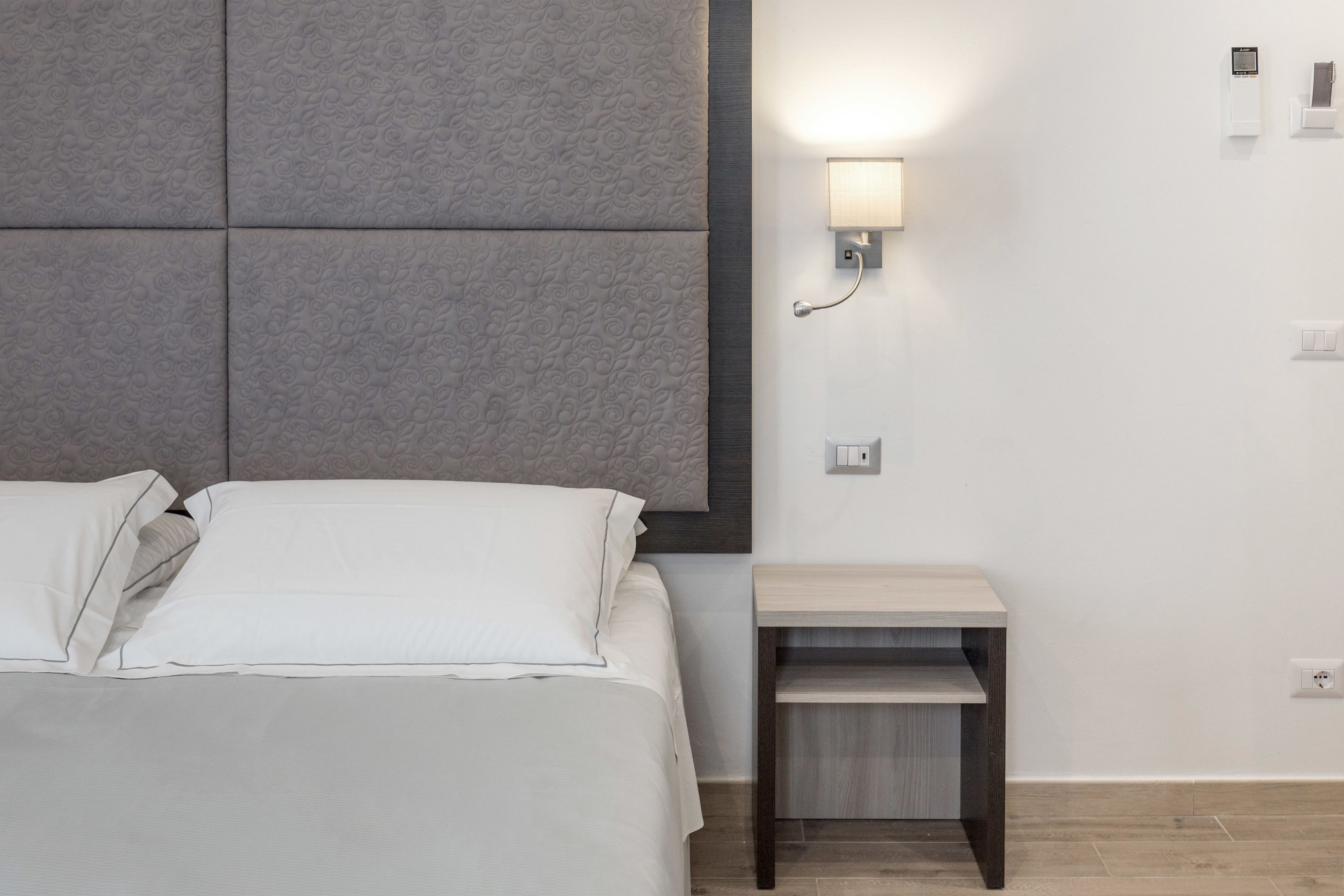 A modern hotel room with a bed, a nightstand, and a wall-mounted light fixture.