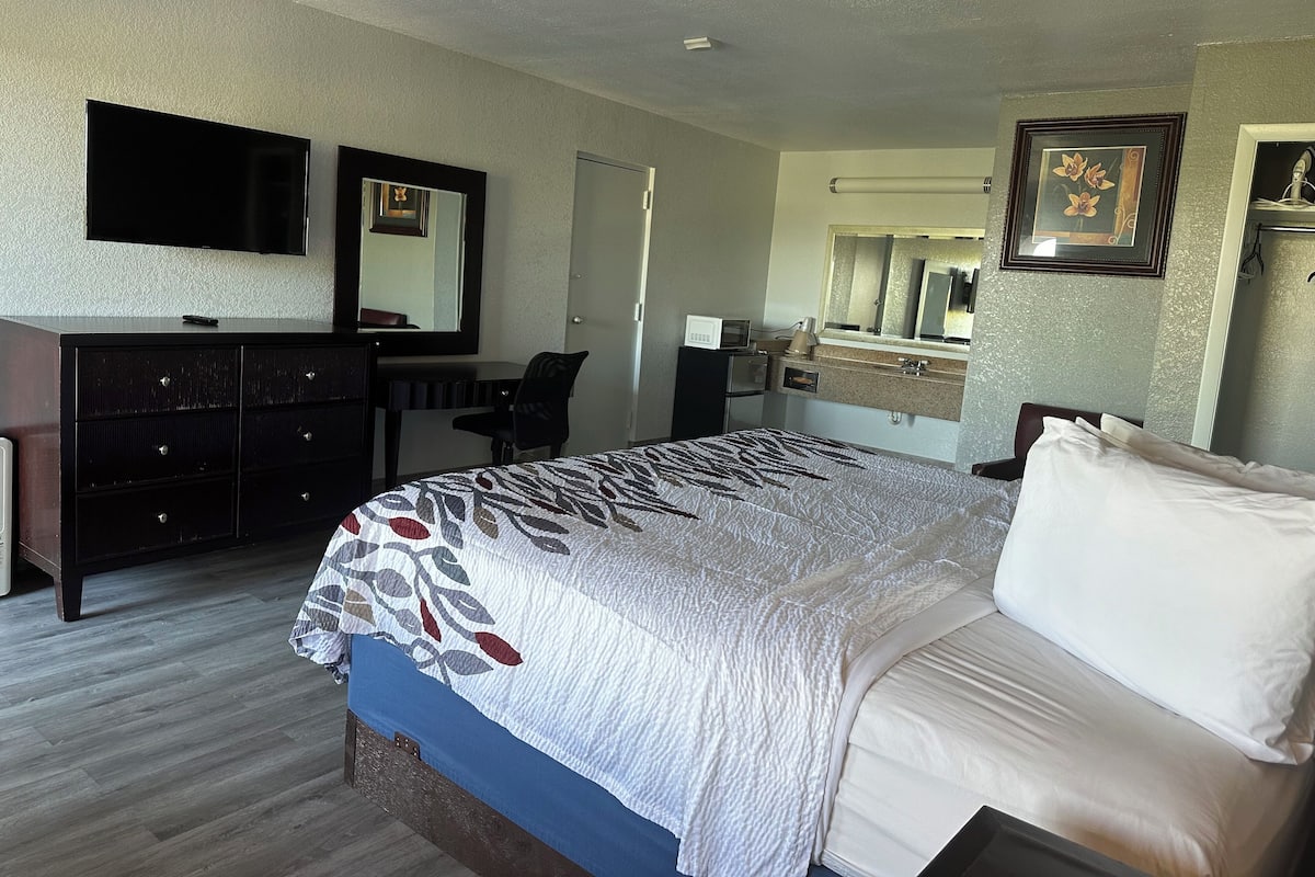 A hotel room with a bed, a dresser, a desk, a chair, a mirror, and a television.