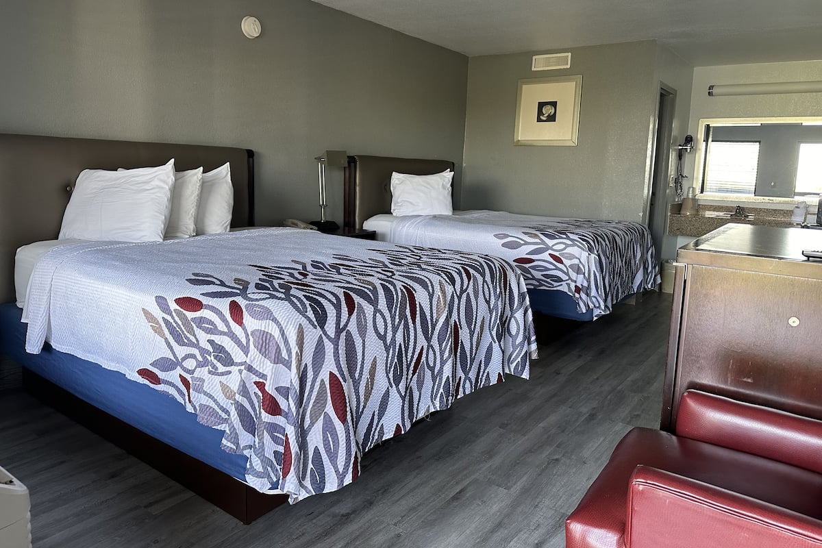 A hotel room with two beds, a desk, and a chair.