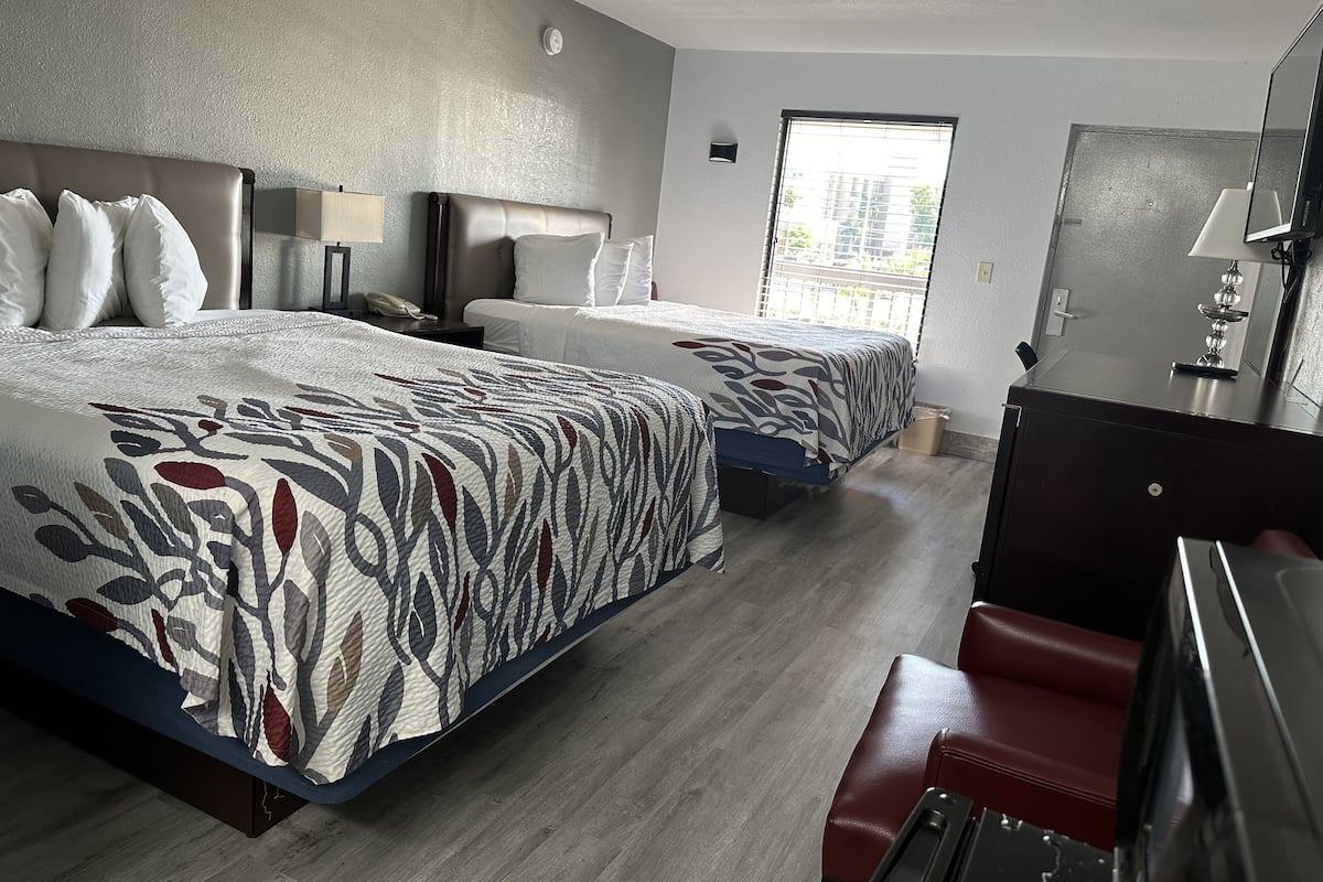 A hotel room with two beds, a desk, a mirror, and a window.