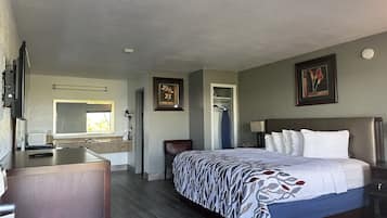 A hotel room with a bed, a desk, a mirror, a wardrobe, and a painting on the wall.