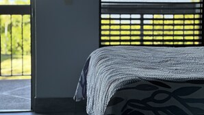 Une chambre à coucher avec un lit, une fenêtre avec des stores et une vue sur la verdure.