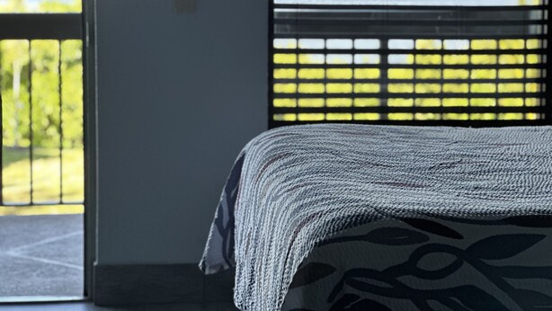 Een slaapkamer met een bed, een raam met zonwering en uitzicht op groen.