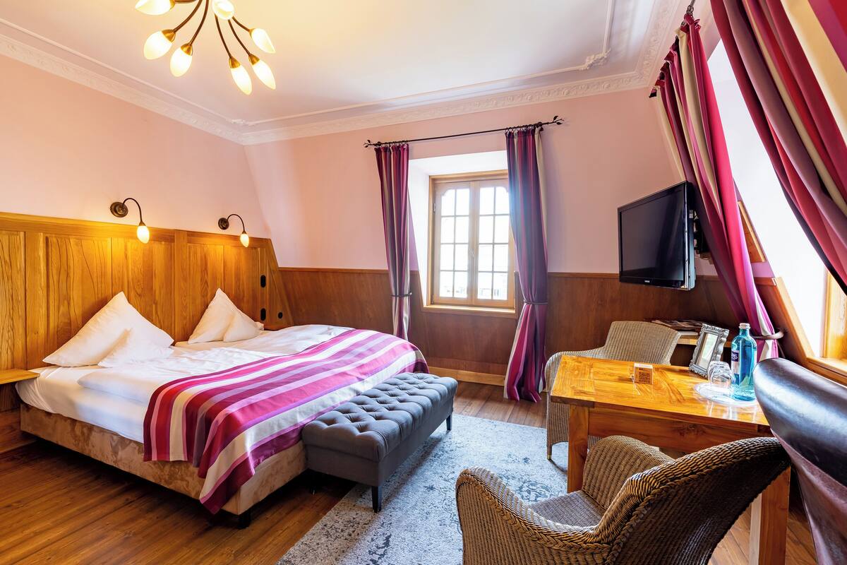 A hotel room with a wooden bed, a small table, a television, and a window with curtains.