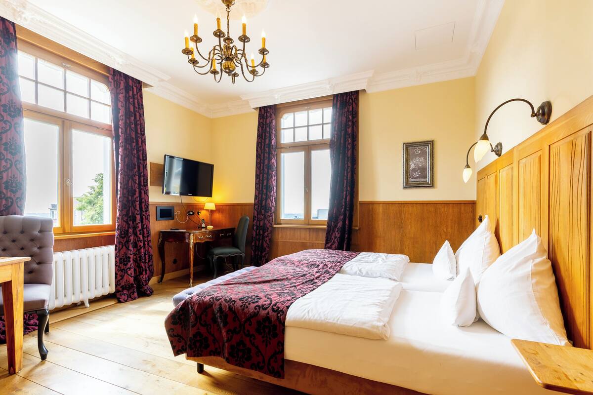 A hotel room with a bed, a desk, a chair, a television, and a window with curtains.