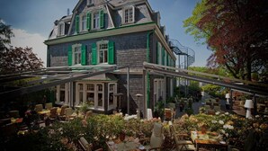 A historic building with a covered outdoor dining area featuring tables and chairs. - Hotel 1782 (Remscheid)