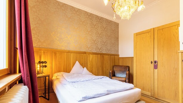 A bedroom with a bed, wooden wardrobe, and a nightstand with a lamp. - Hotel 1782 (Remscheid)