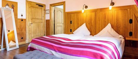 Quarto com uma cama grande, um banquinho, um espelho e painéis de madeira nas paredes.
