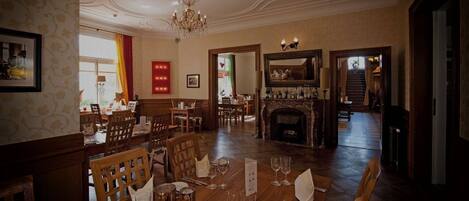 A dining area with wooden tables and chairs, a chandelier, and a fireplace.