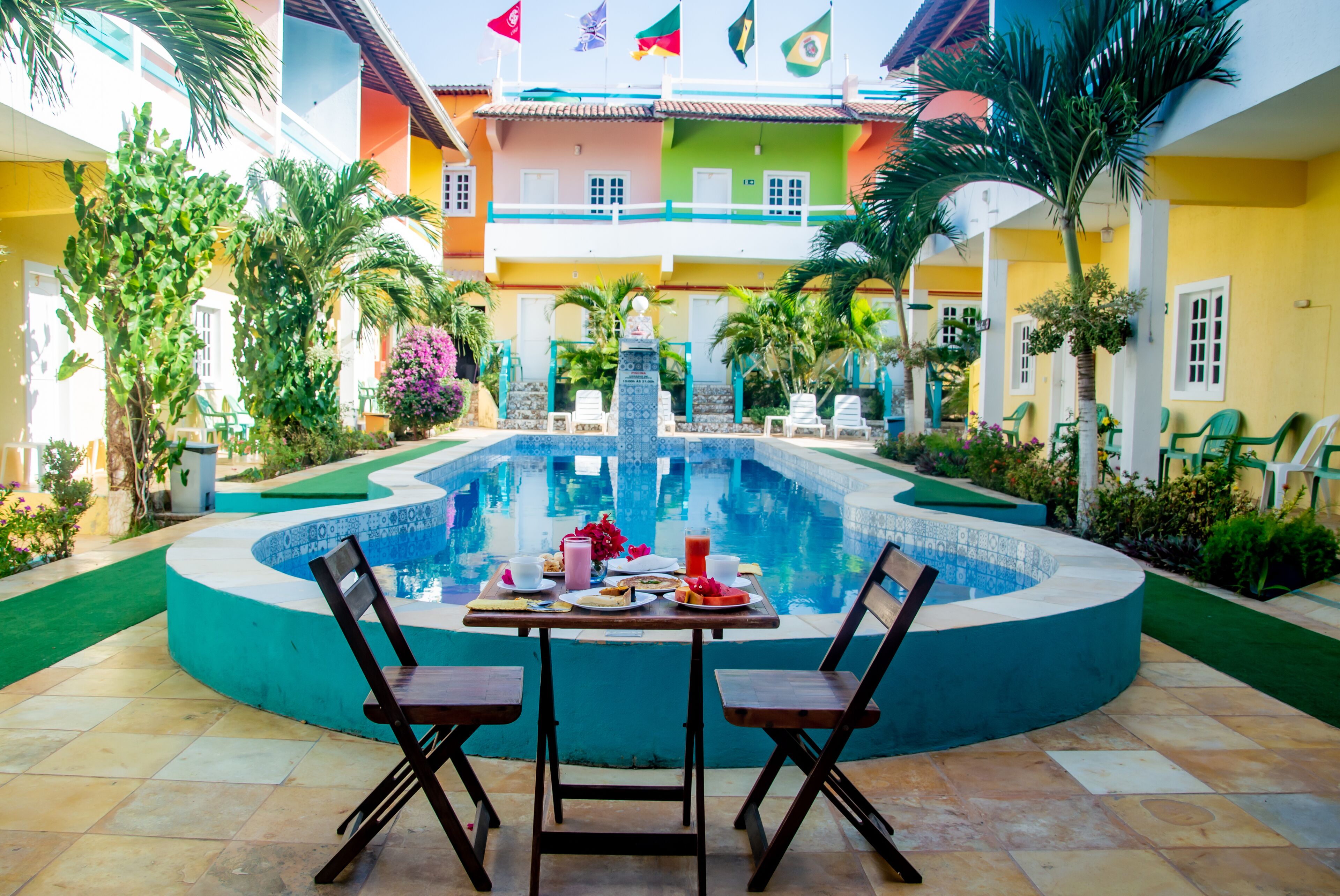 A pool area with a table and chairs, surrounded by colorful buildings and palm trees.