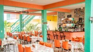 Un restaurante con sillas y mesas anaranjadas, una zona de bar y una escalera.