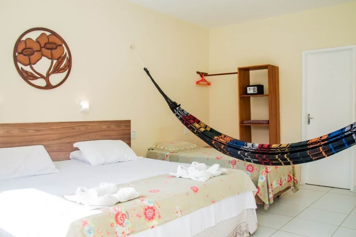 A hotel room with two beds, a hammock, a wall decoration, and a shelf with a radio.