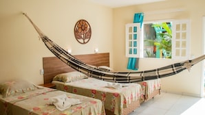 Habitación con dos camas, una hamaca, cabecera de madera, un adorno en la pared y una ventana con cortinas.