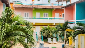 Un edificio colorido con varias banderas, un balcón y un patio con sillas y plantas.
