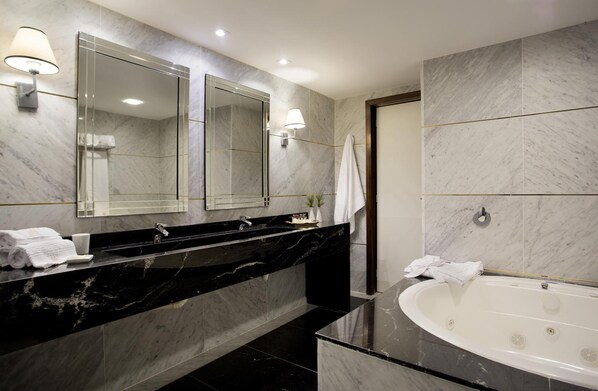 A modern bathroom with a black marble vanity, a large mirror, a bathtub, and a towel rack. - Royal Atlântica Macaé Hotel (Macaé)