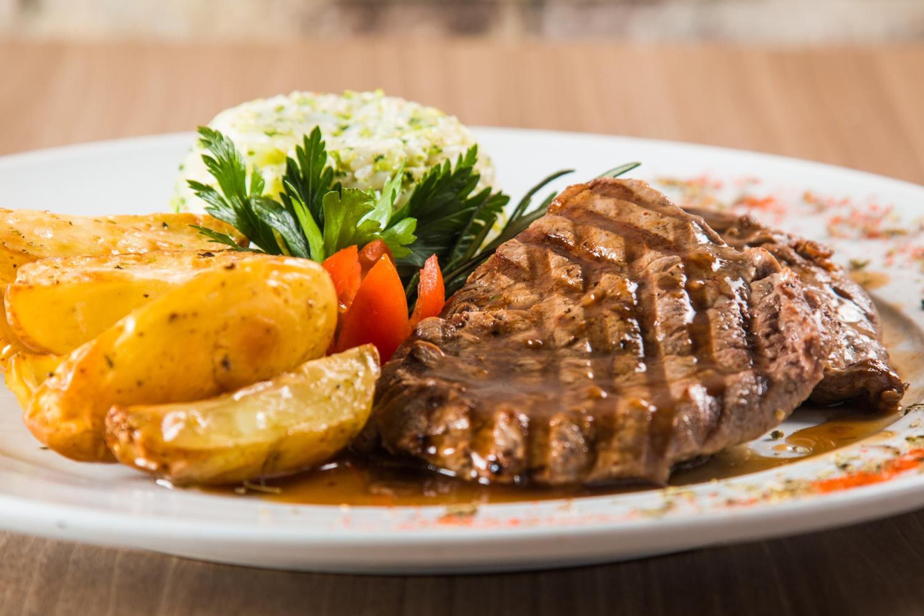 Une assiette comprenant un steak, des pommes de terre rôties et une portion de purée de pommes de terre garnie d’herbes.