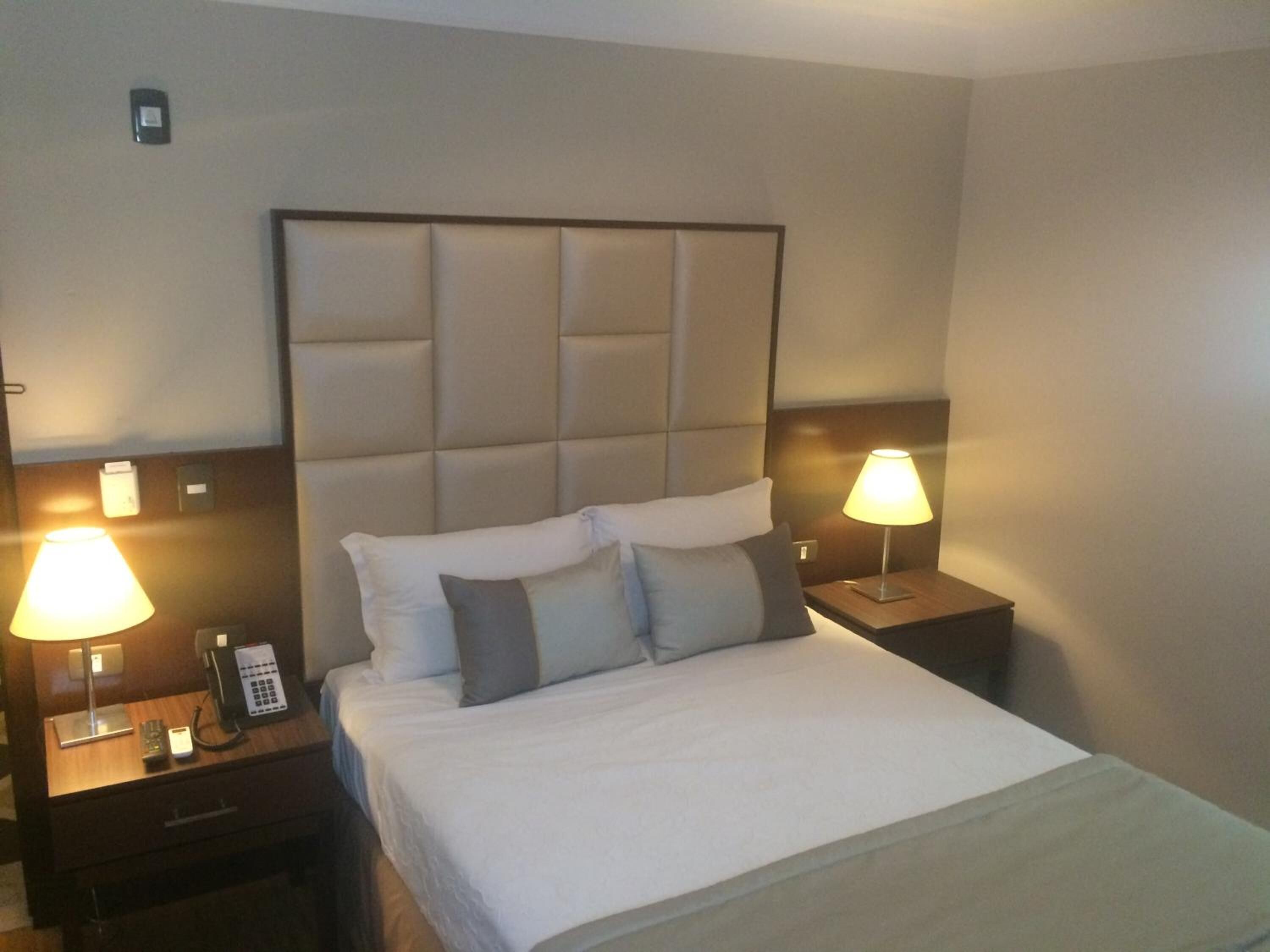 A hotel room with a large bed, two bedside tables with lamps, a phone, and a small drawer.
