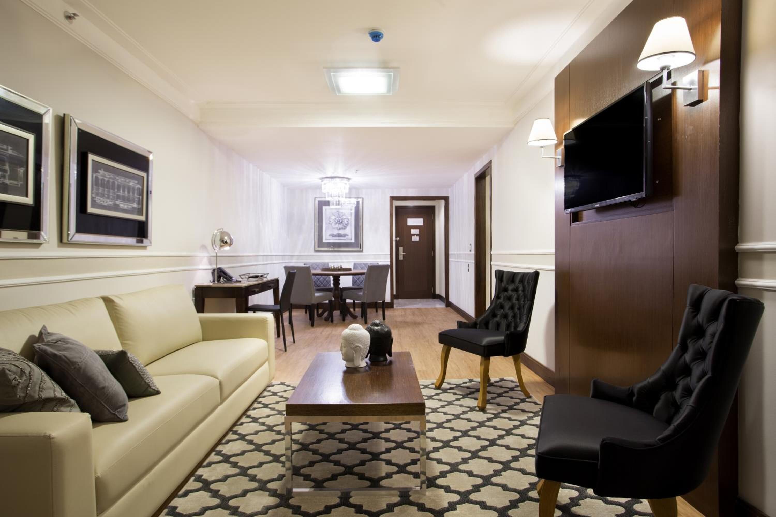 A hotel room with a sofa, armchair, coffee table, TV, and framed pictures on the wall.
