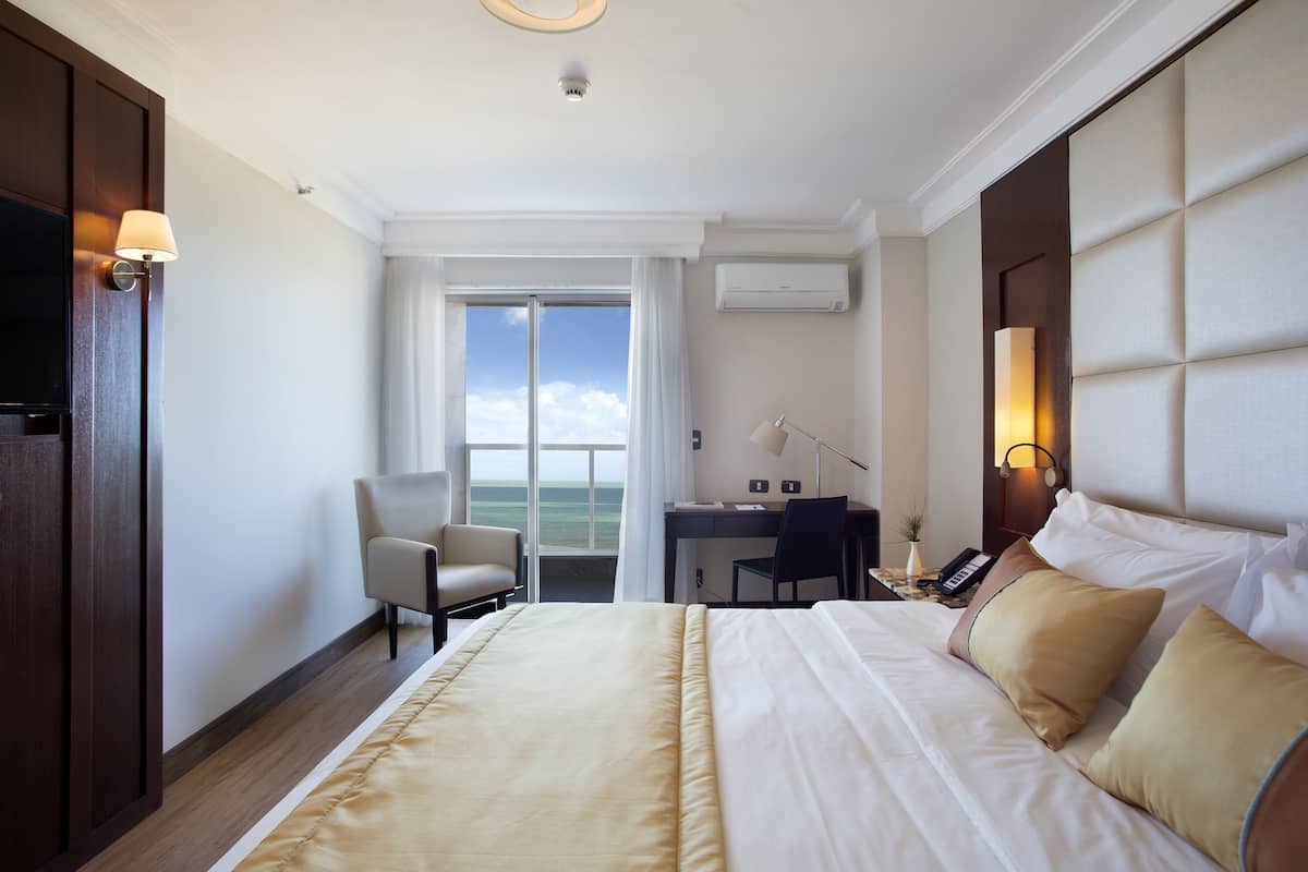 A hotel room with a bed, desk, chair, and a view of the outdoors.