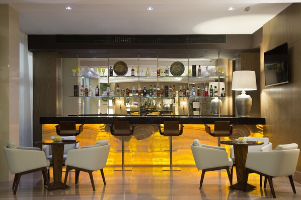A modern bar area with a long counter, multiple stools, and a variety of bottles and glasses. - Royal Atlântica Macaé Hotel (Macaé)