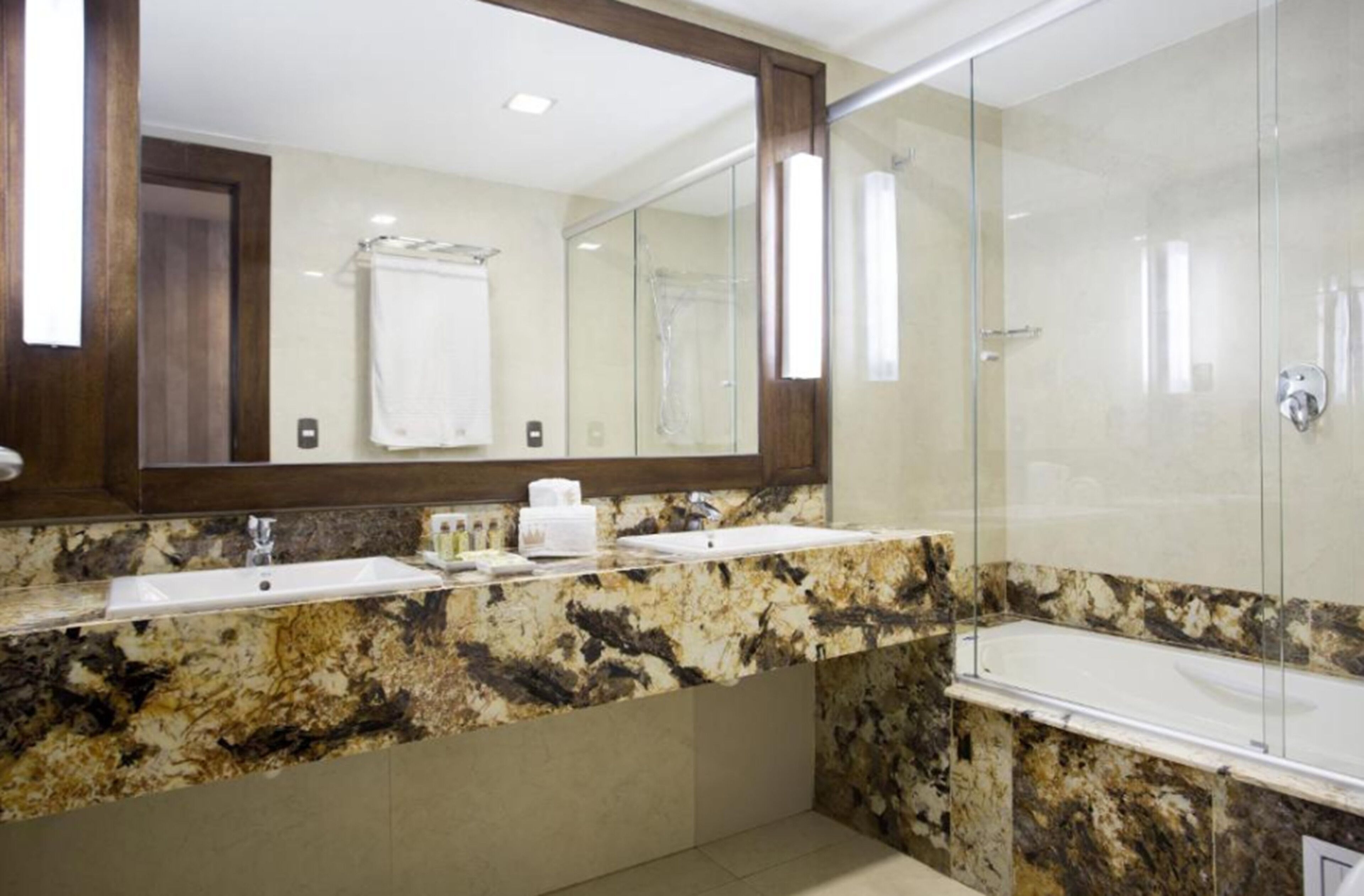 Un baño con dos lavamanos, un espejo grande y una ducha con mampara de vidrio.