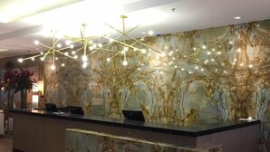 A reception desk with a marble-patterned wall, a modern chandelier, and a clean, polished floor. - Royal Atlântica Macaé Hotel (Macaé)