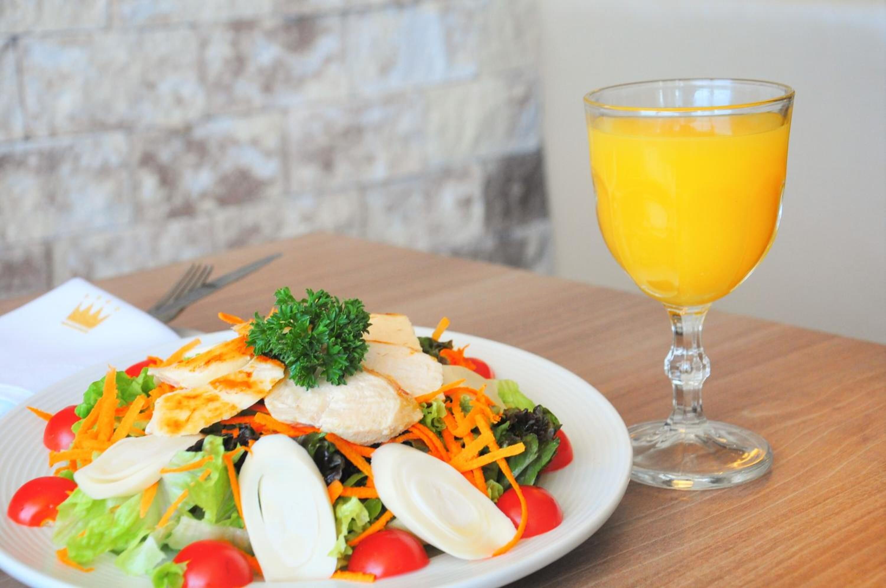 Une assiette de salade composée de poulet, de laitue et de tomates cerises, ainsi qu'un verre de jus d'orange, le tout posé sur une table en bois.