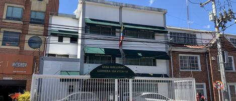 Un edificio con un letrero que dice "Casa Guillermo" y una entrada porticada con dos coches estacionados adentro.