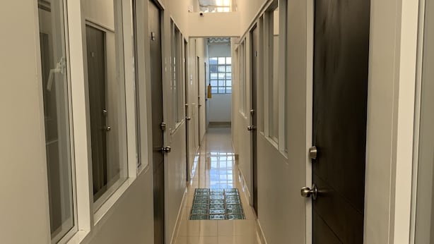 Un pasillo largo y estrecho con puertas a ambos lados, que conduce a una habitación luminosa al final.